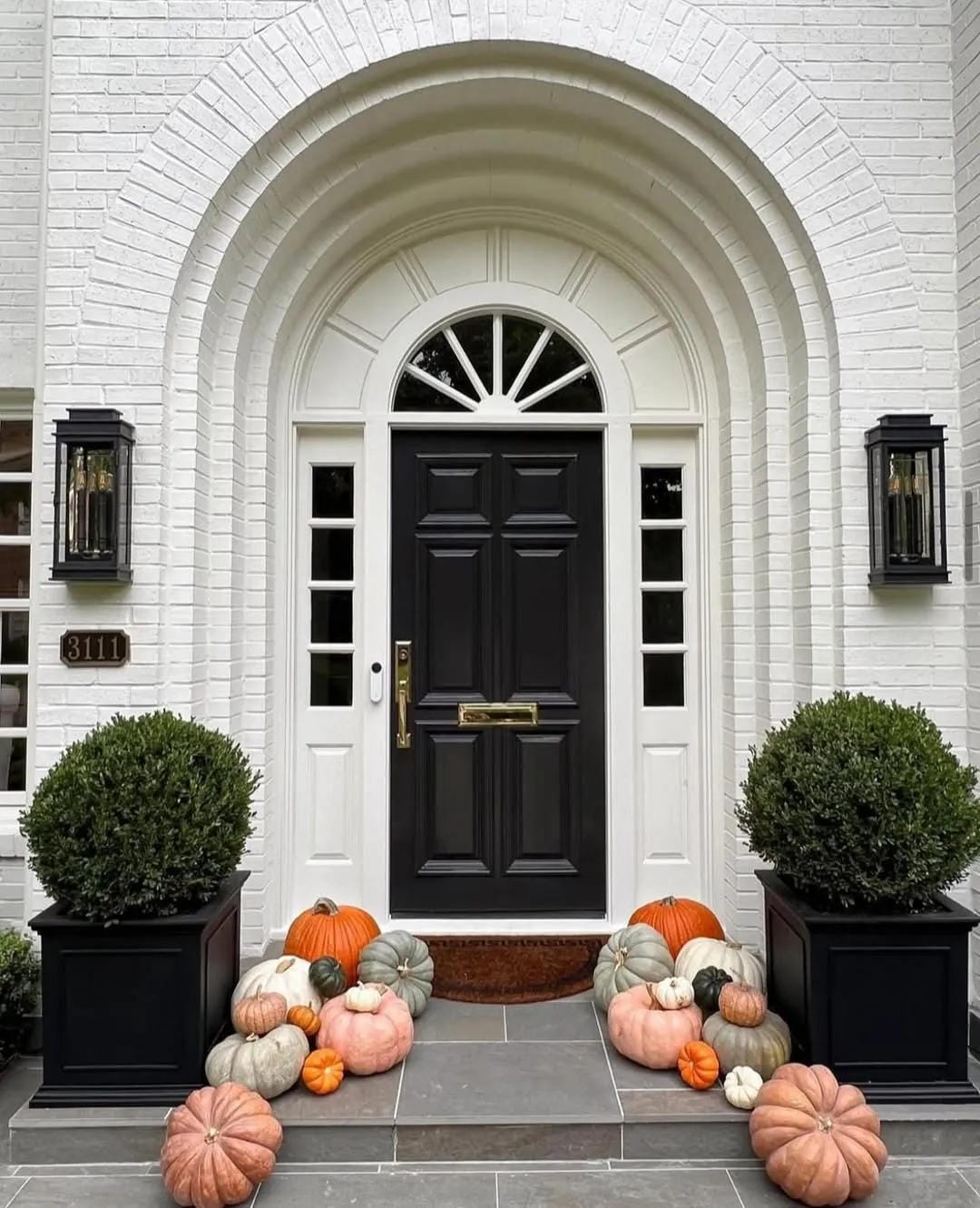 fall front door decor ideas with white brick entry, black door, and pumpkins lining the steps