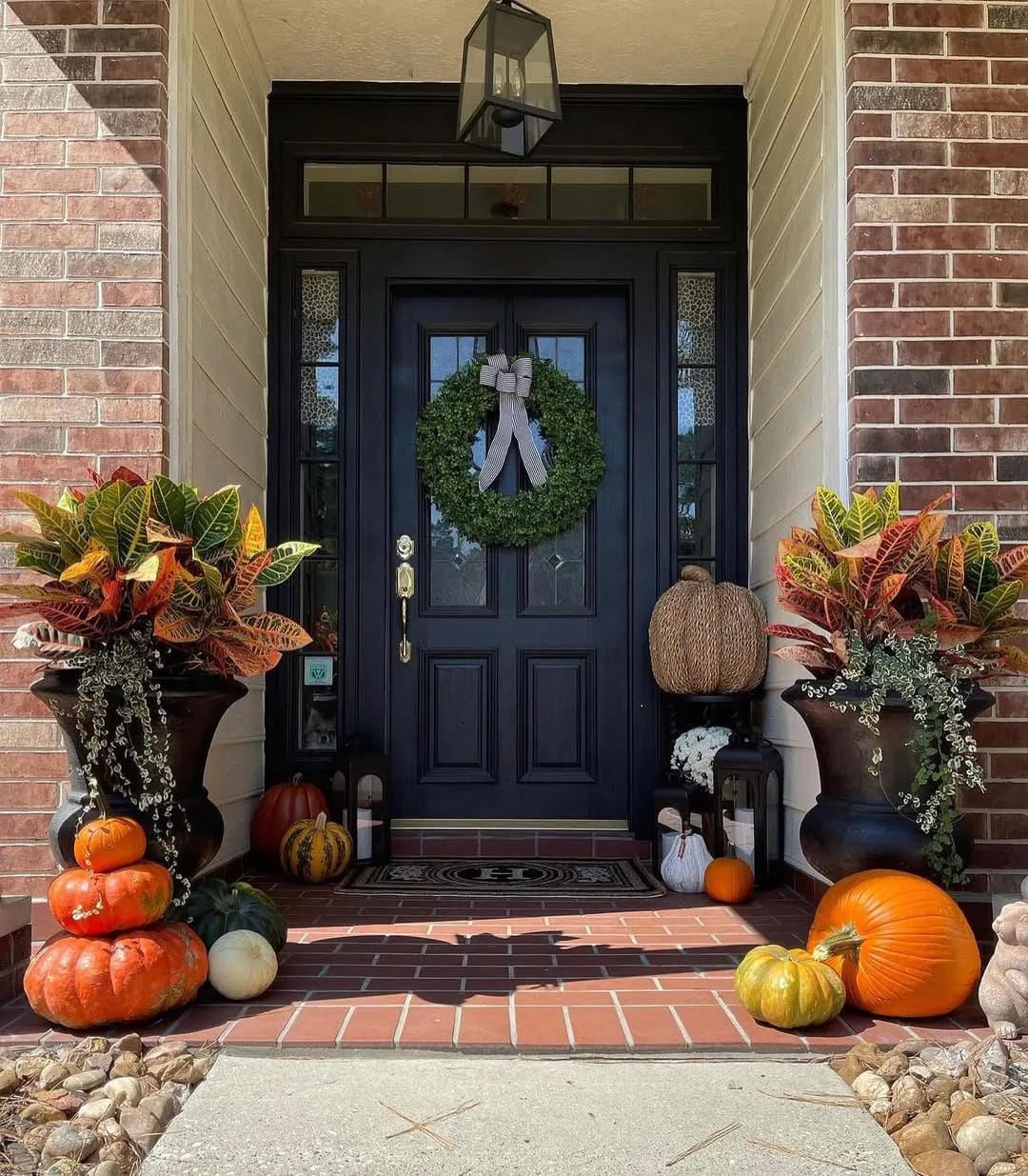 fall front door decor ideas with black door, tall planters, pumpkins, fall flowers, and wreath
