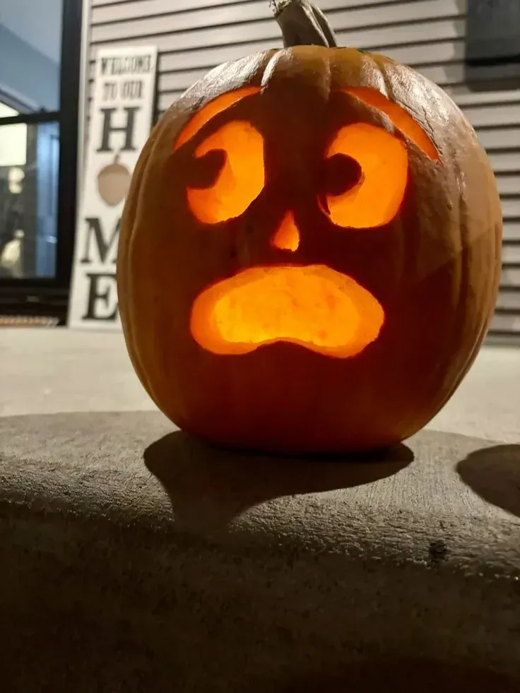 kid friendly pumpkin carving ideas with sad pumpkin face, big glowing eyes, and simple mouth