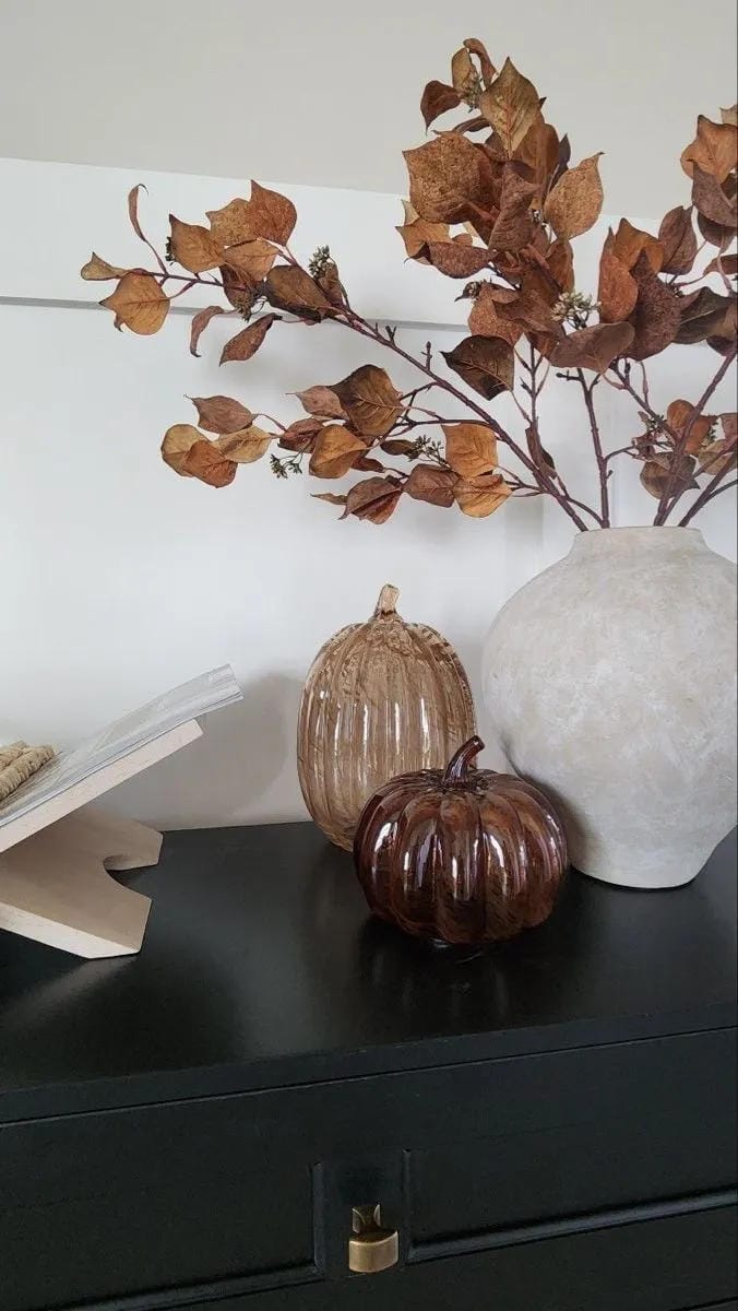 fall entryway table decor ideas with sculptural vase, warm autumn leaves, glass pumpkin, and black console table