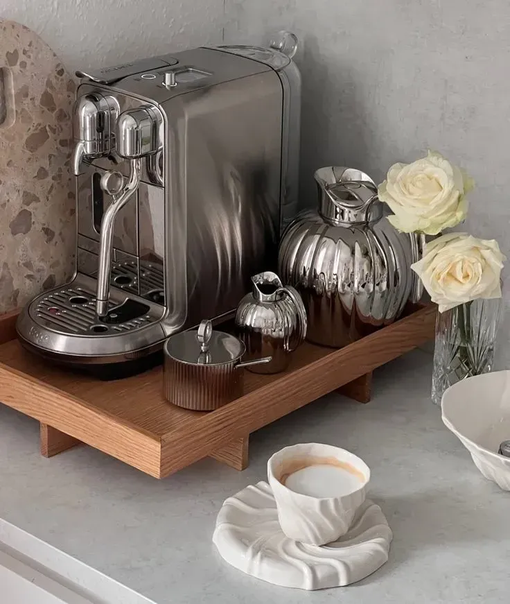 coffee station ideas with silver espresso machine, silver accessories, wooden tray, white roses, and white cup