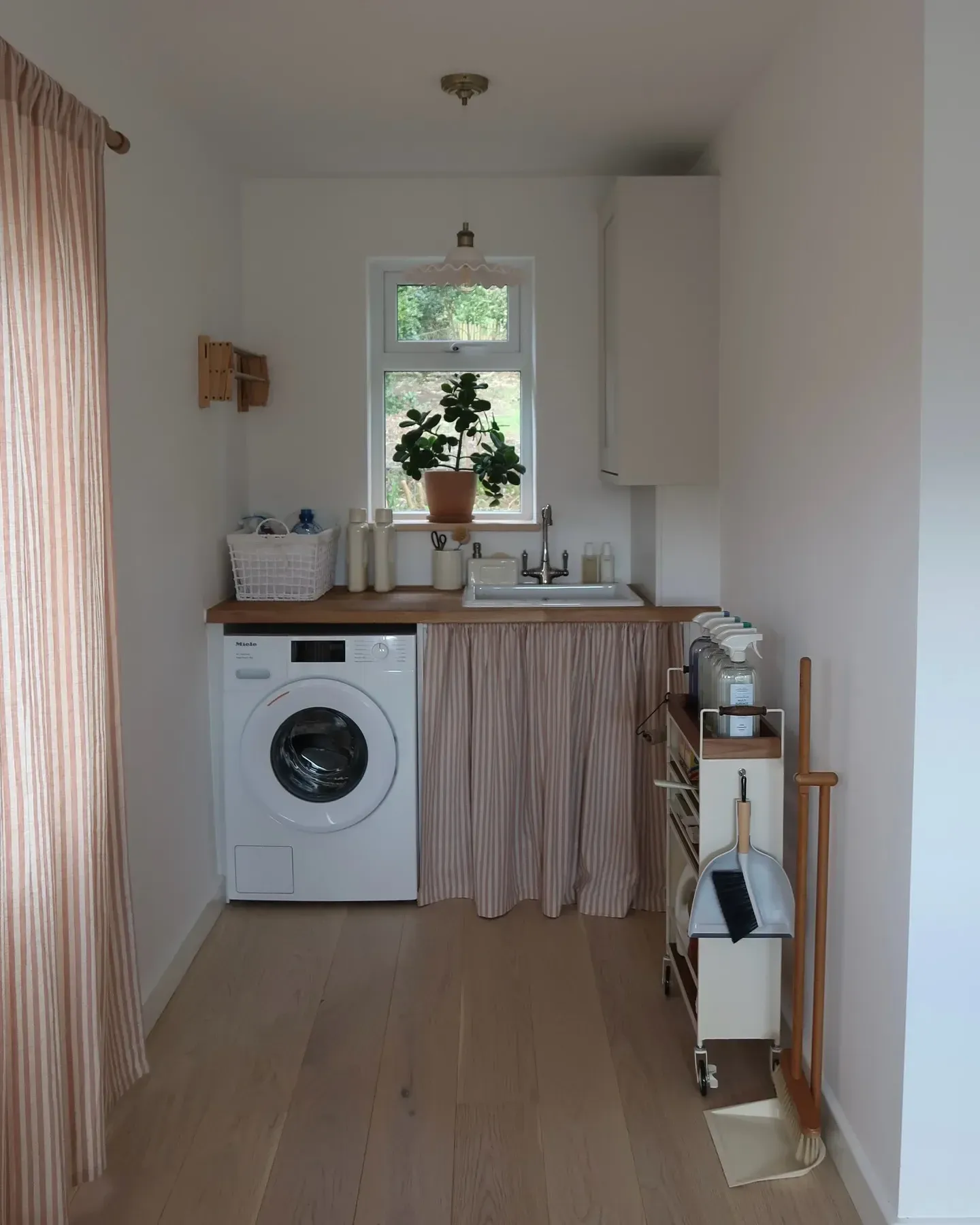 small laundry room ideas with skirted sink, washer, curtain storage, wood counter, and narrow laundry layout