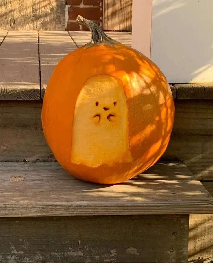 kid friendly pumpkin carving ideas with baby ghost pumpkin, rounded cutout, tiny face, and glowing light