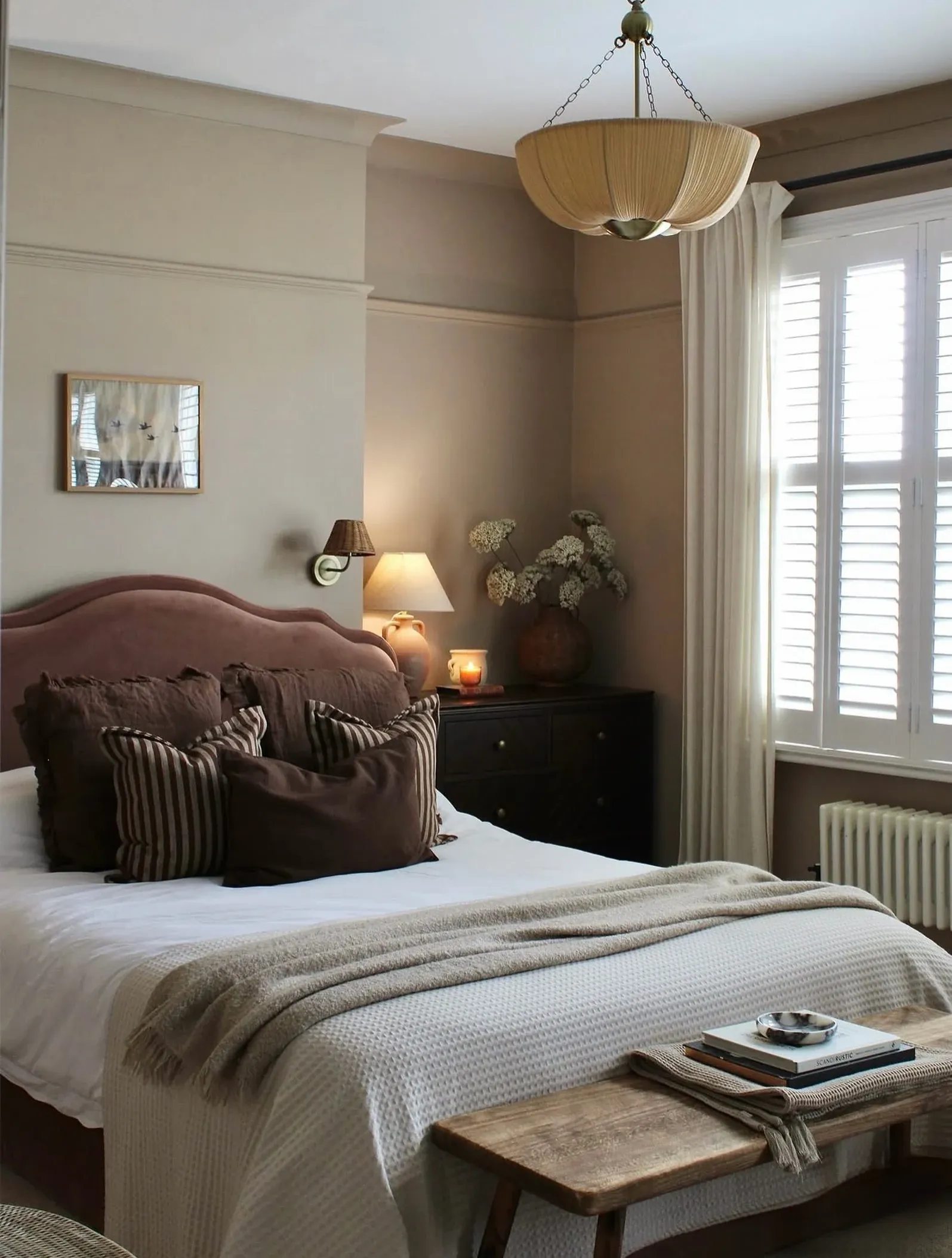 fall bedroom ideas with small vase of fall leaves, brown pillows, warm bedside lamp, neutral bedding, and cozy bedroom bench