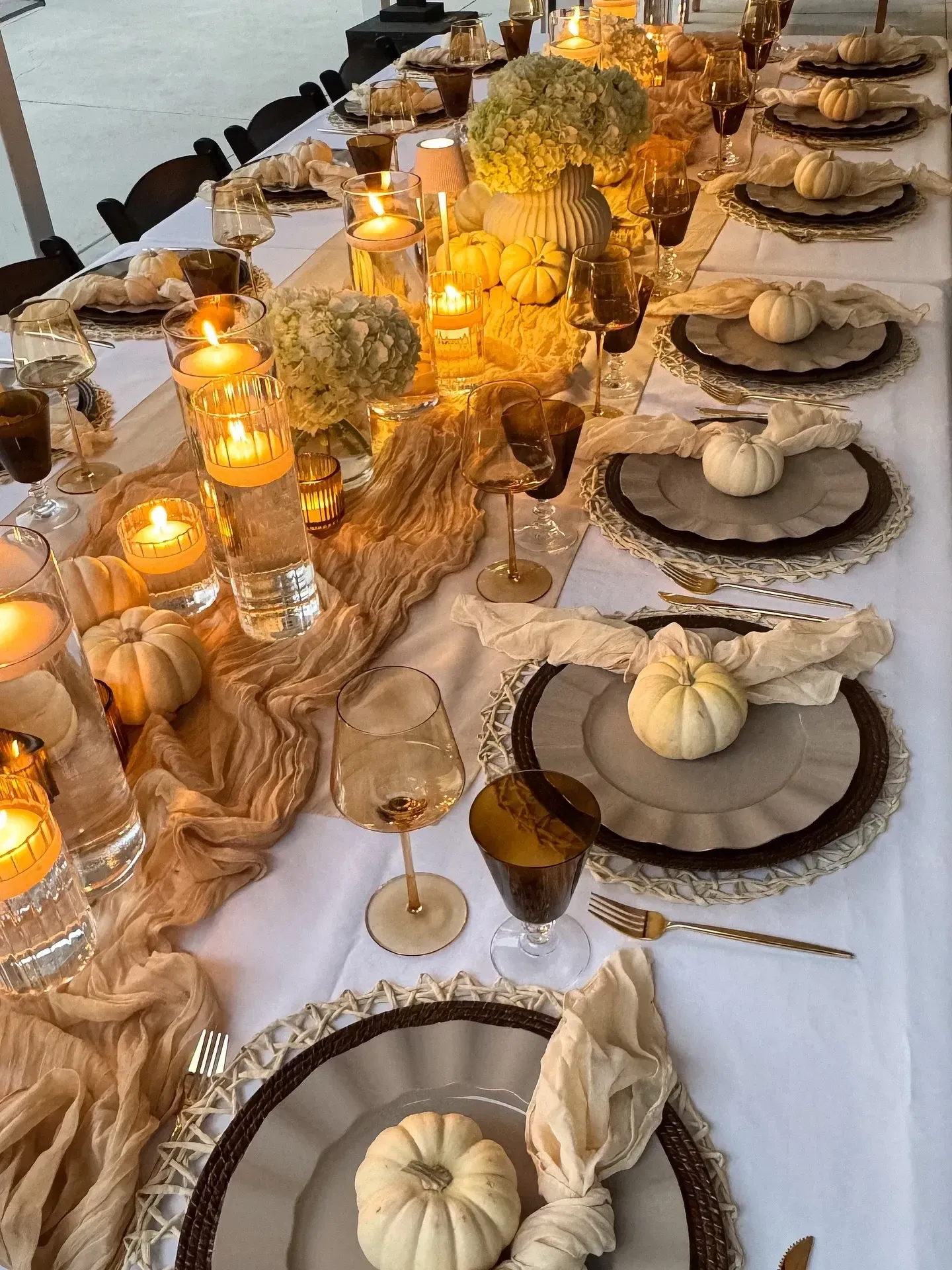 fall table decor ideas with candlelight, gauzy runner, white pumpkins, amber glasses, and layered place settings