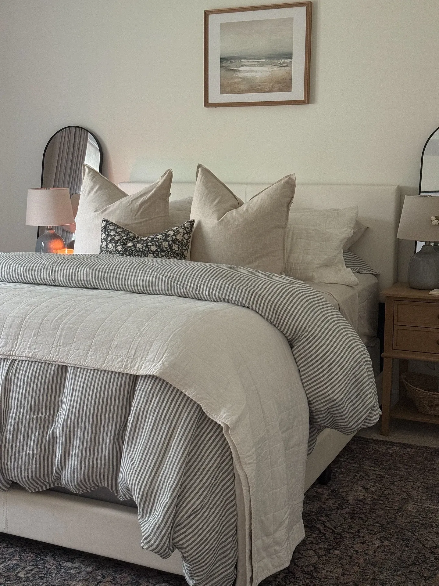 fall bedroom ideas with soft bedding, striped bed skirt, olive pillow, woven bench, and framed artwork