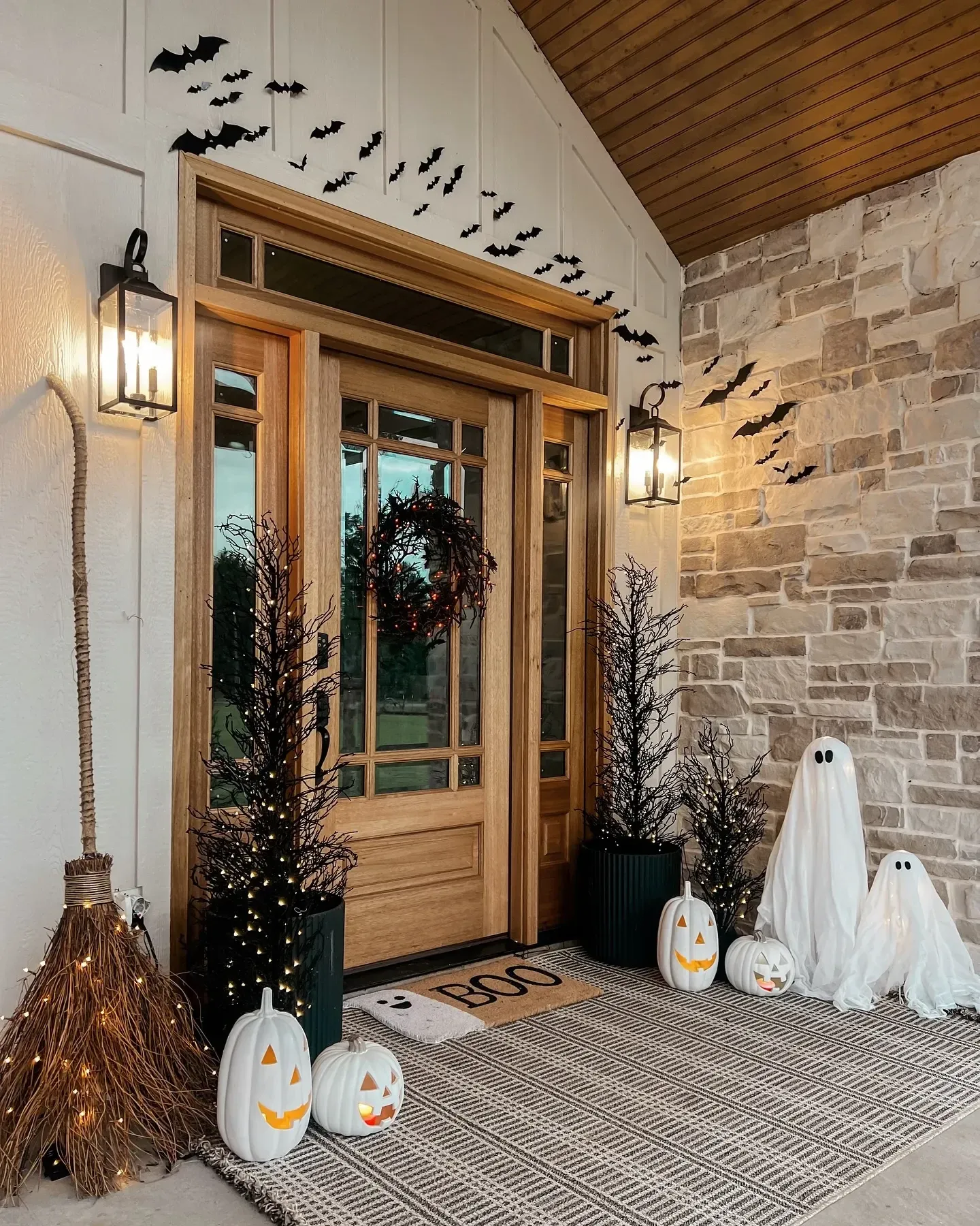 fall porch decor ideas with Halloween bats, ghost decor, broom, jack-o-lanterns, black trees, wreath, and layered porch rug