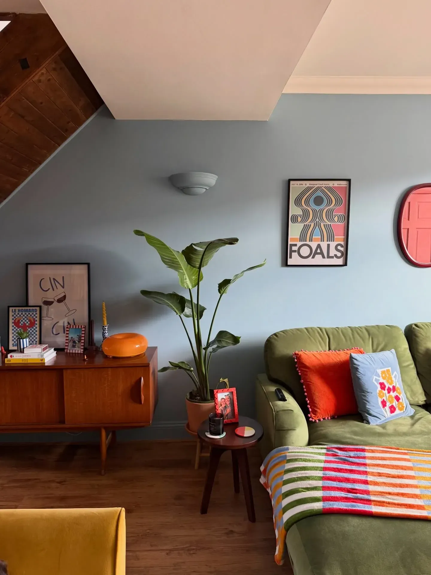 colorful living room ideas with green armchair, red round mirror, striped throw, plant, and mid century cabinet