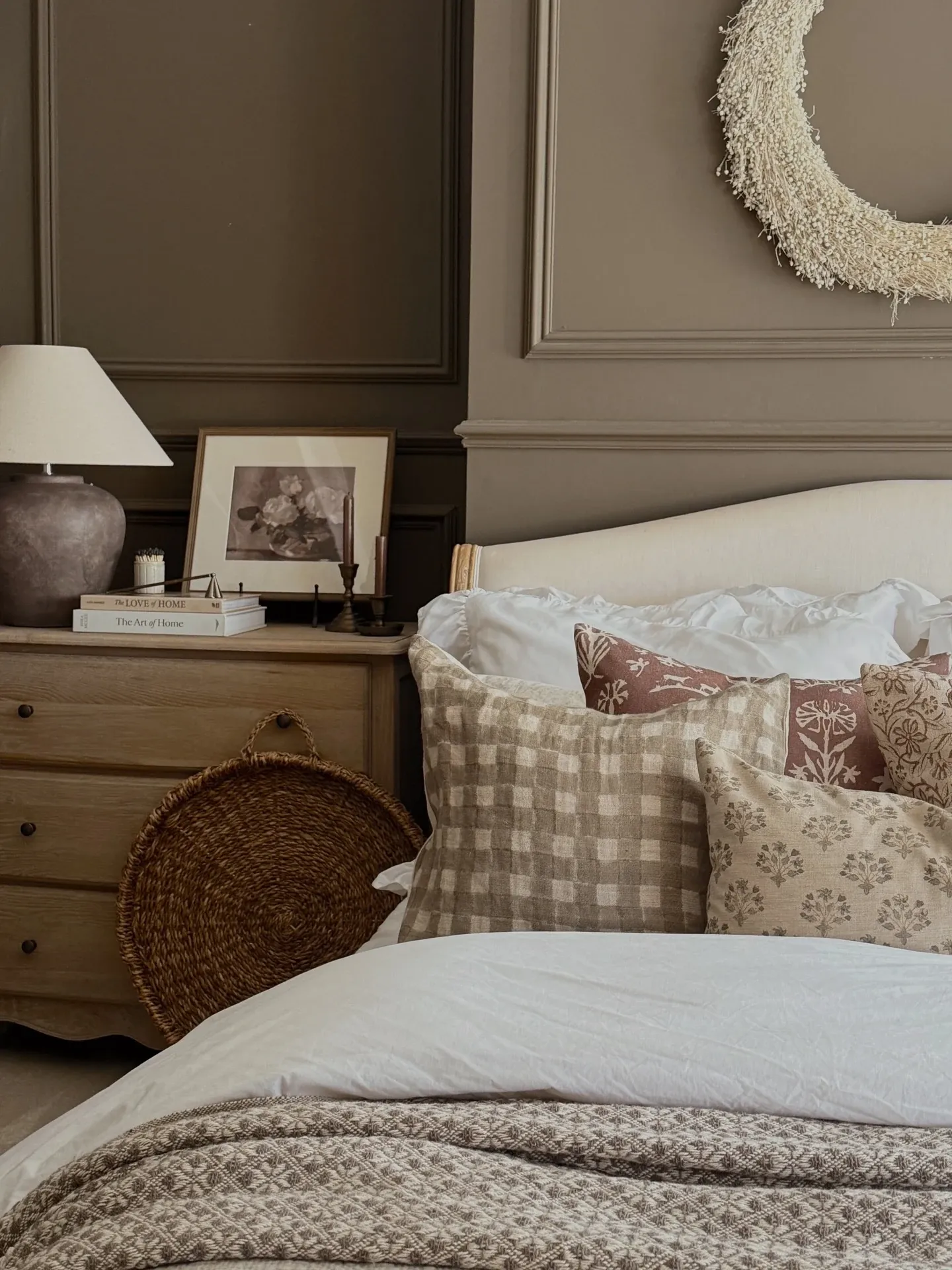fall bedroom ideas with subtle wreath, moody wall, checked pillow, floral cushion, wood nightstand, and neutral bedding