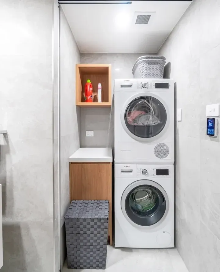 small laundry room ideas with stacked washer dryer, tall hamper, open shelf, compact cabinets, and small laundry storage