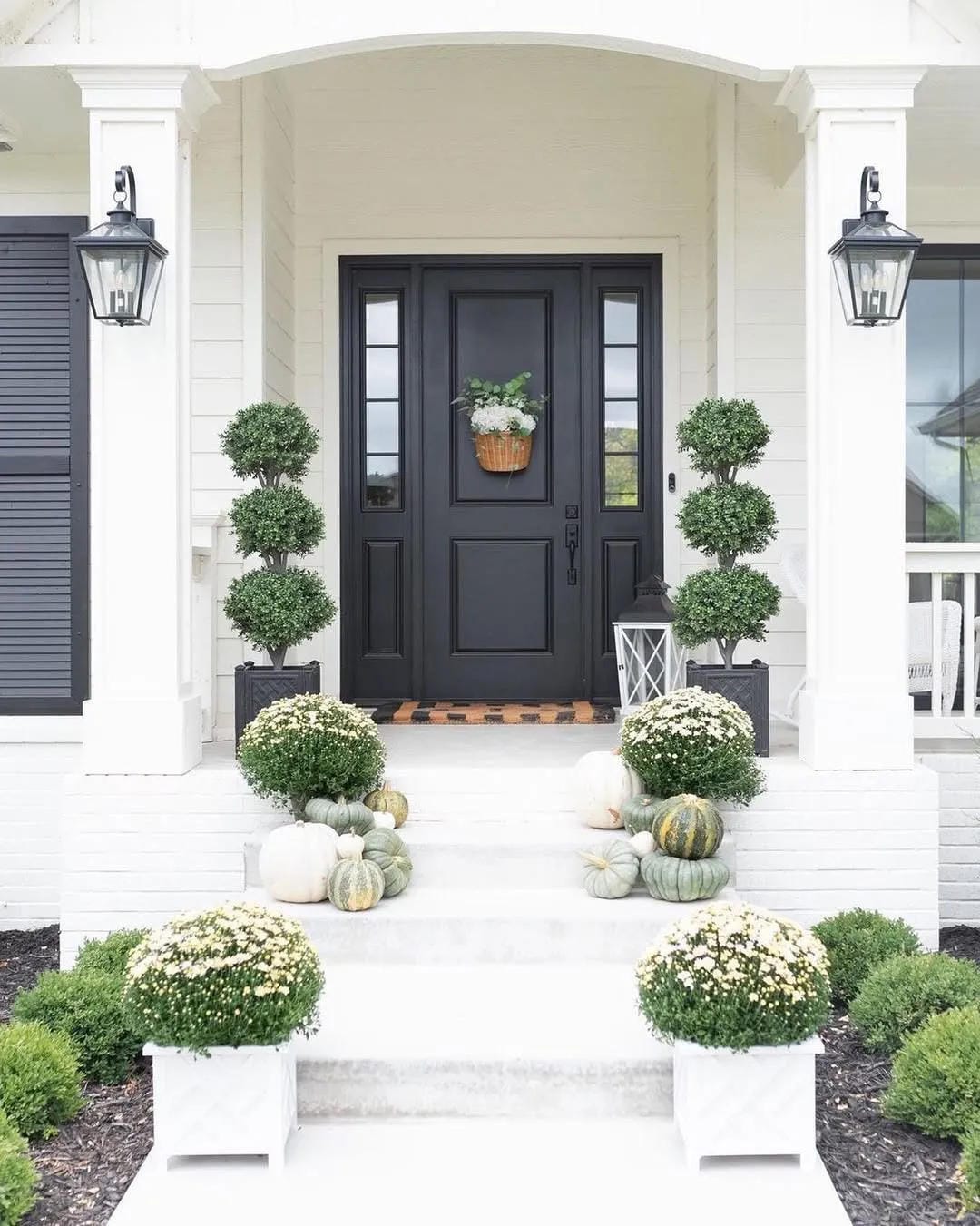 fall front door decor ideas with black door, topiaries, white pumpkins, white flowers, and classic porch steps