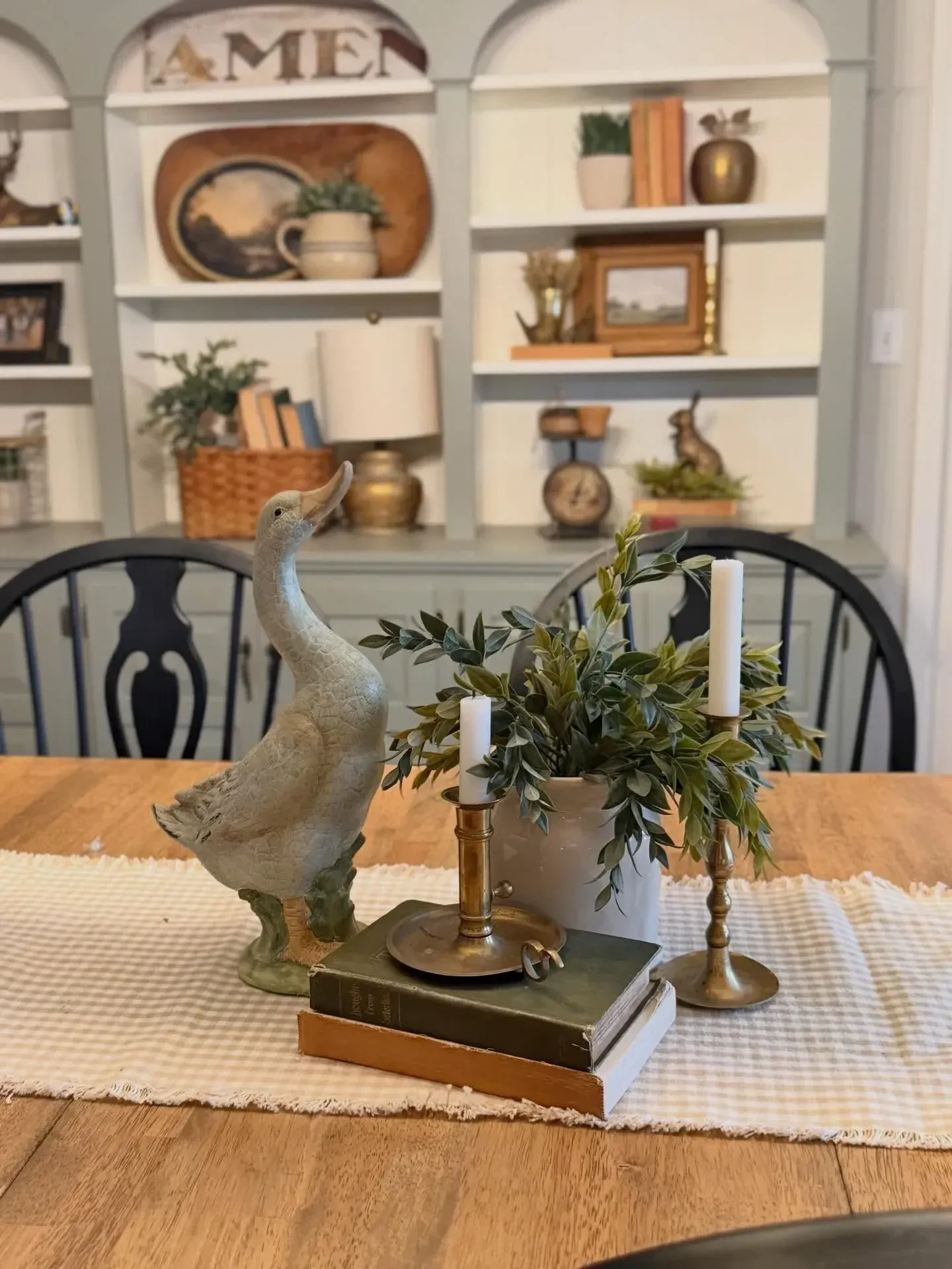 vintage home decor ideas with table centerpiece, brass candlesticks, old books, greenery, and decorative goose