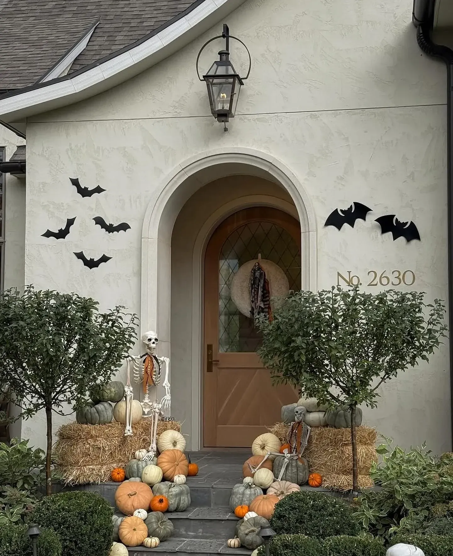 fall porch decor ideas with Halloween bats on the wall, pumpkins, hay bales, skeleton decor, and arched front door