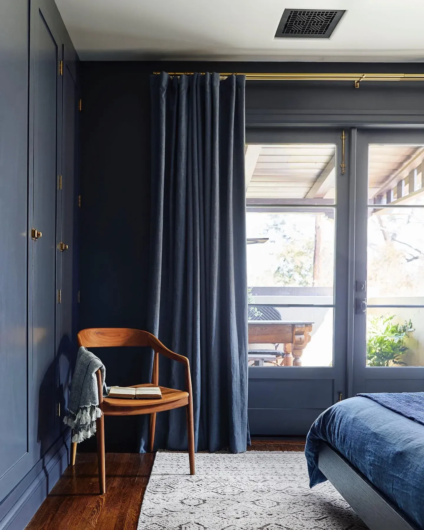 moody bedroom ideas with navy curtains, blue built ins, wood chair, and dark bedroom window