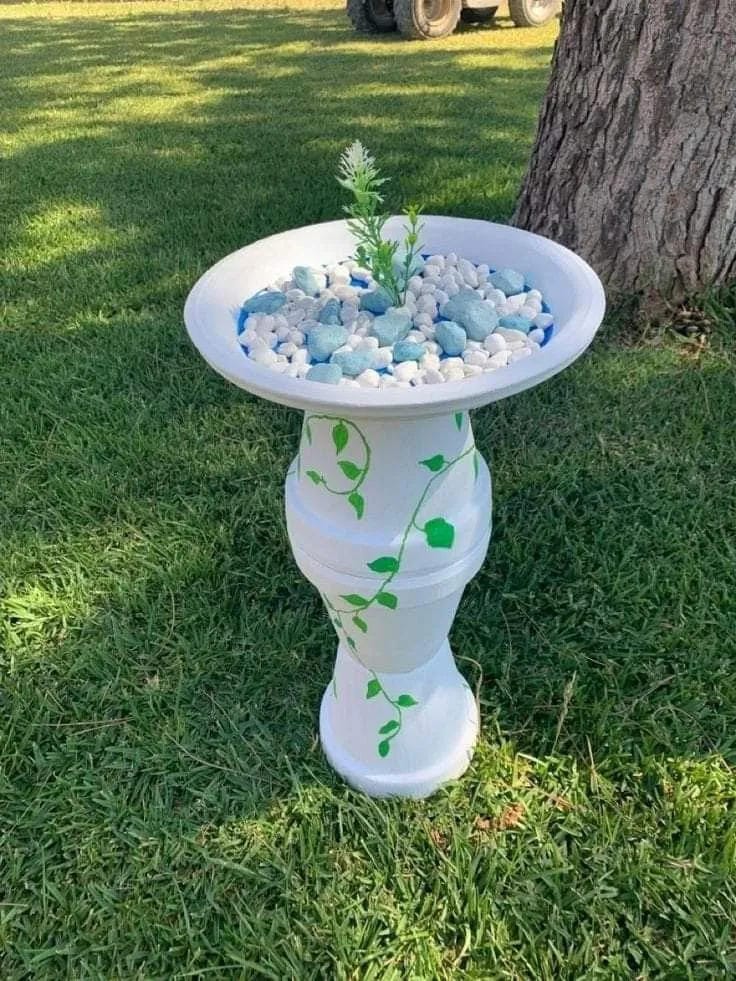 DIY bird bath idea with white pedestal, green vines, pebbles, and small plant
