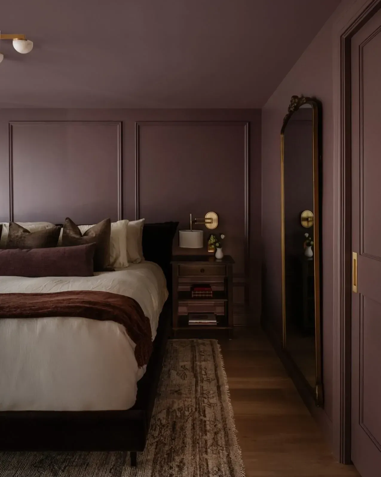 moody bedroom ideas with plum paneled walls, long runner rug, vintage mirror, and layered bedding