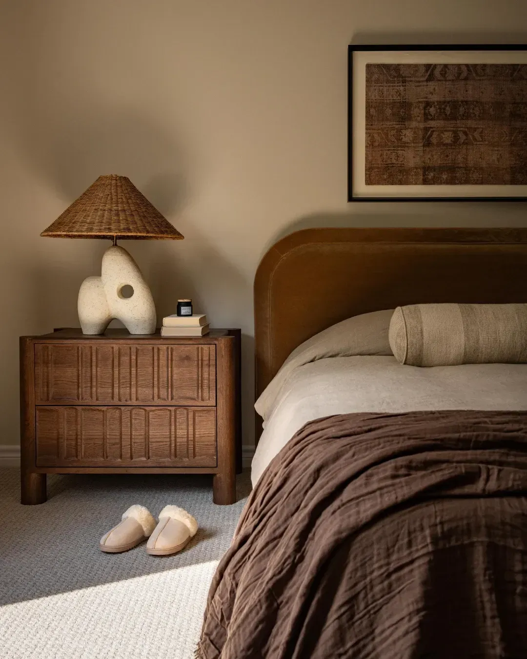 moody bedroom ideas with wood nightstand, curved headboard, brown throw, woven lamp, and framed textile art