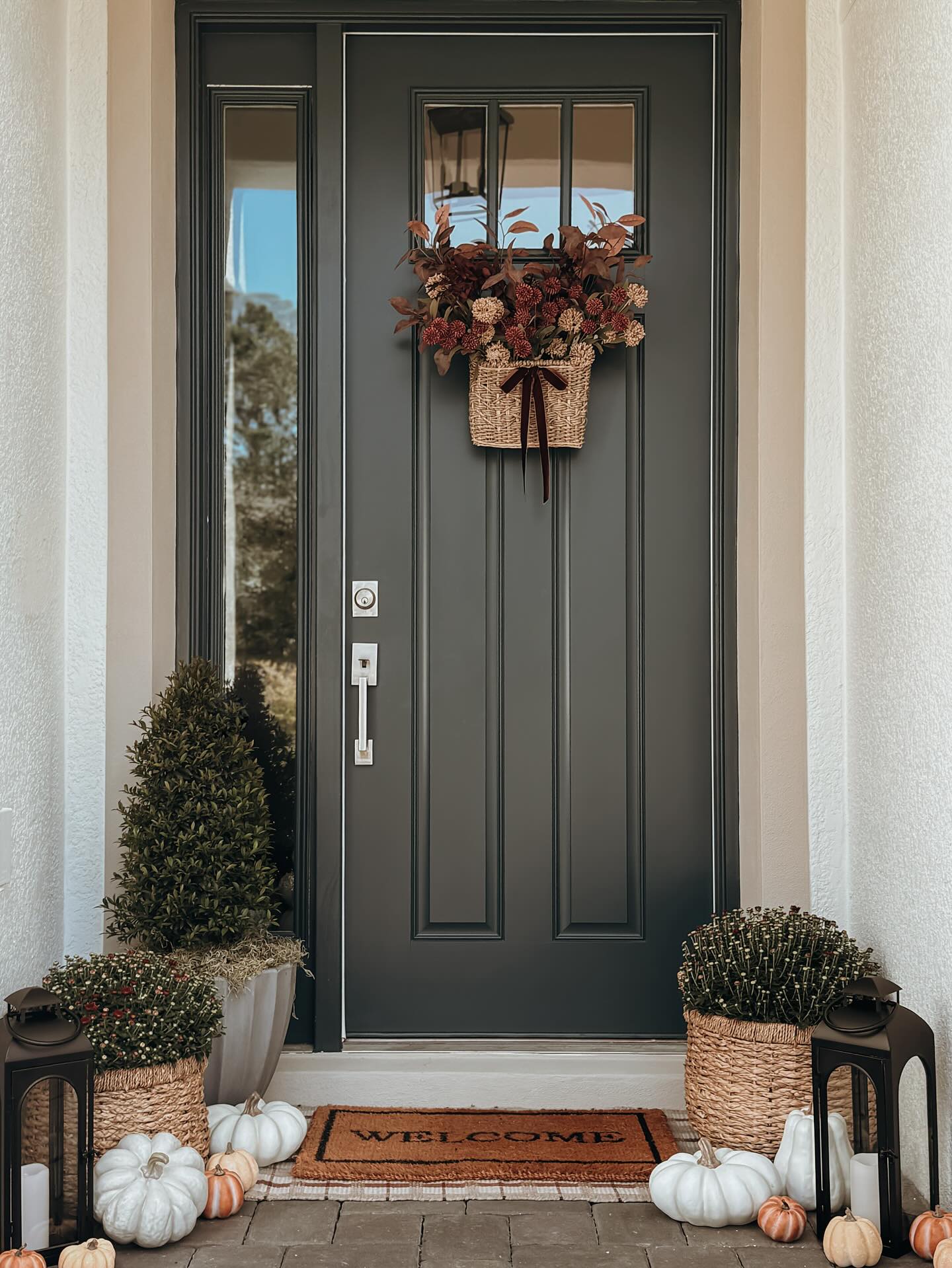 fall porch decor ideas with a woven door basket, fall stems, basket mums, lanterns, white pumpkins, and welcome mat