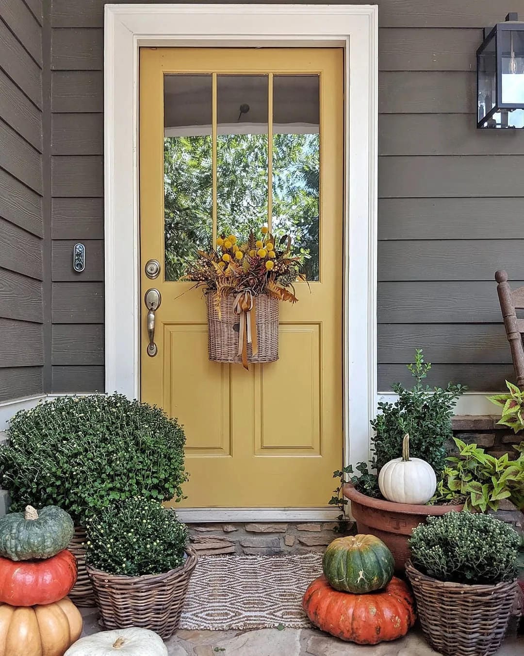 fall front door decor ideas with yellow door, hanging basket, pumpkins, plants, and layered doormat